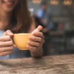 Jovem mulher alegre ao beber chá quente sentada à mesa