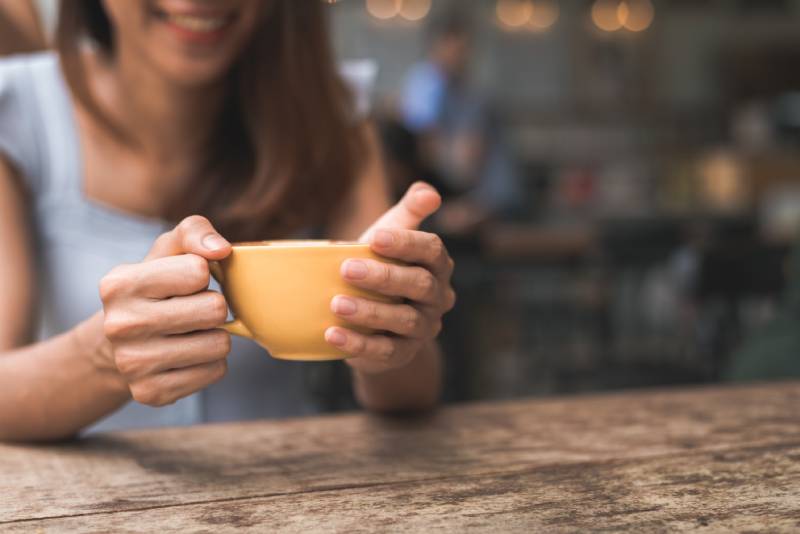 Jovem mulher alegre ao beber chá quente sentada à mesa