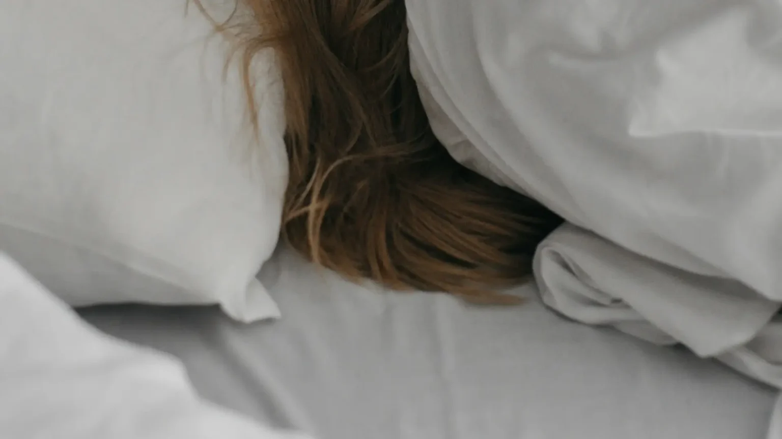 a woman is hiding under a blanket on a bed